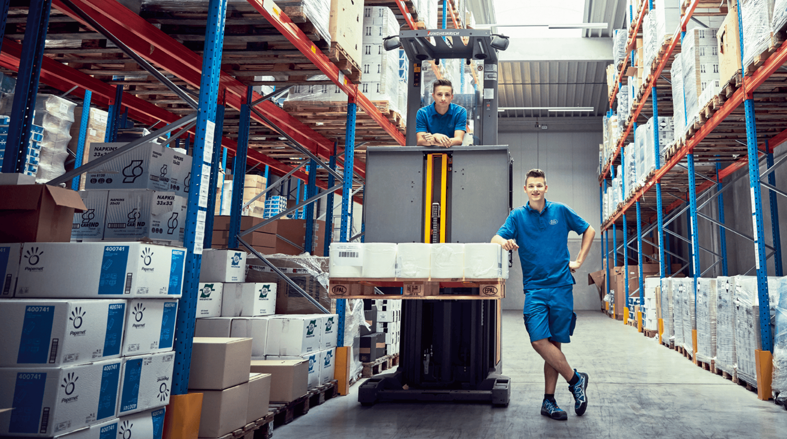 Zwei Lagermitarbeiter. Einer sitzt im Gabelstapler